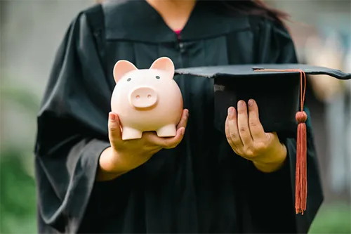 Graduate holding piggy bank and grad cap